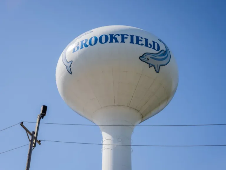 Large white water tower with "BROOKFIELD" and dolphin logos against a clear blue sky.