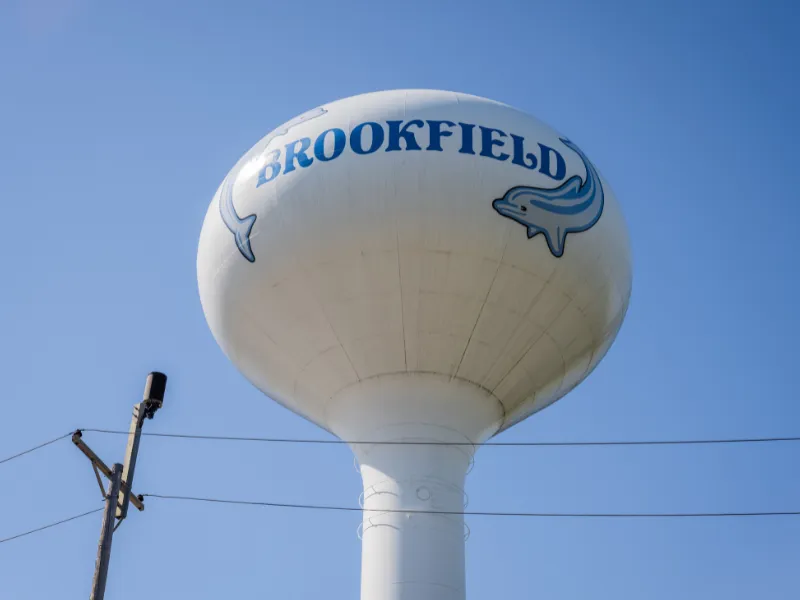 Large white water tower with "BROOKFIELD" and dolphin logos against a clear blue sky.
