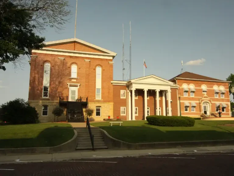 Historic brick courthouse building with white columns and a green lawn in front.