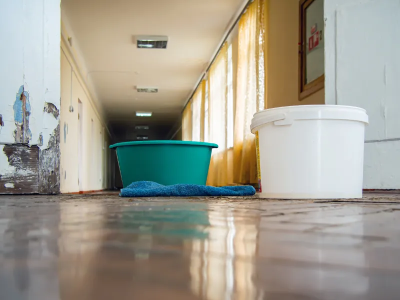 Two plastic buckets and a blue cloth on a shiny tiled floor in a hallway with yellow curtains.