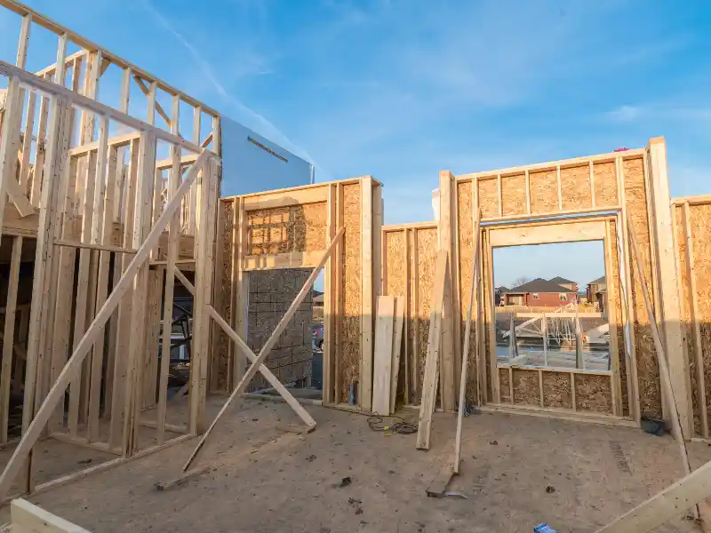 Wooden framing and plywood walls of a house under construction with a clear blue sky.