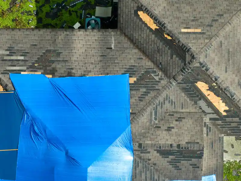 Roof with damaged shingles covered partially by a blue tarp.