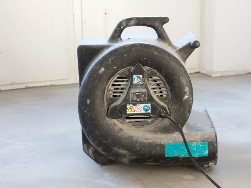 Black industrial blower fan with a handle and power cord on a concrete floor.
