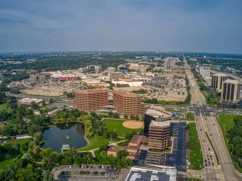 Aerial view of a suburban office park with multiple buildings, a pond, and a baseball field.